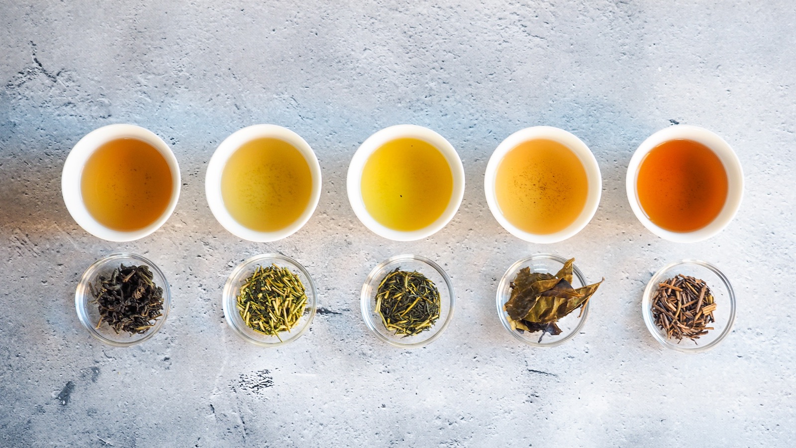 Five white cups of mirume hojicha in a row, each with a small glass dish of its dry tea below.