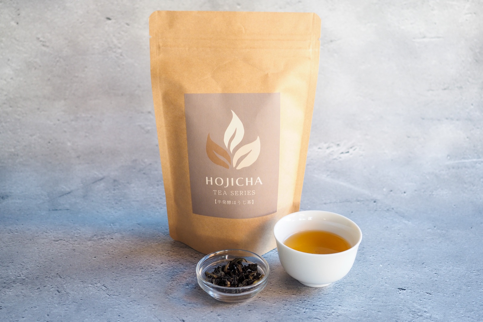 The tea bag package of No.4 Oolong Hojicha, with a small glass dish of the dry tea and a white cup of the brewed tea.